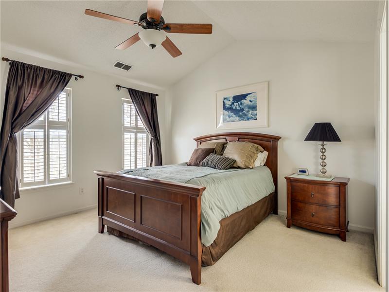 The master bedroom features plantation blinds, vaulted ceiling and fan