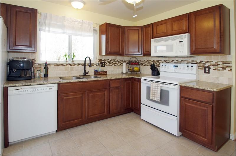 Kitchen with new cabinetry, backsplash, tile flooring, smooth top stove, and granite counters